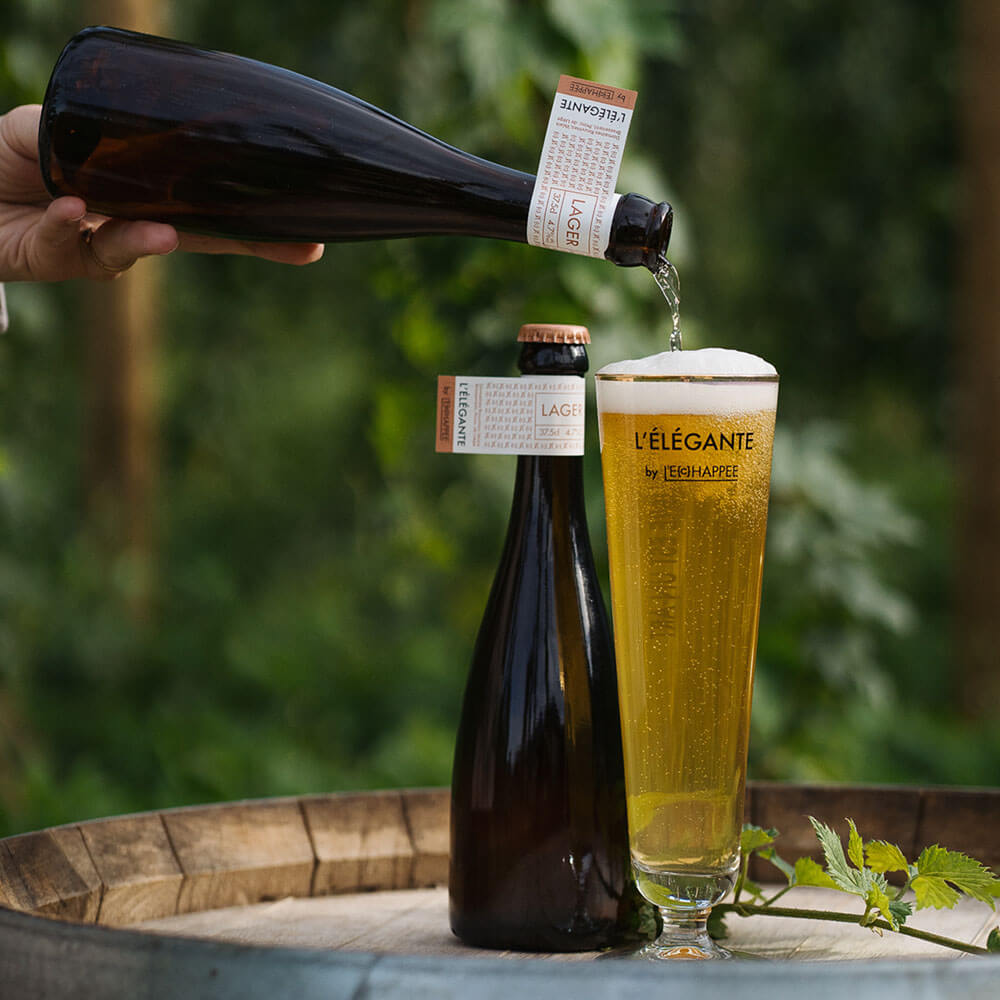 Bière elegante avec le verre sur un tonneau avec le champs de houblon en arrière plan